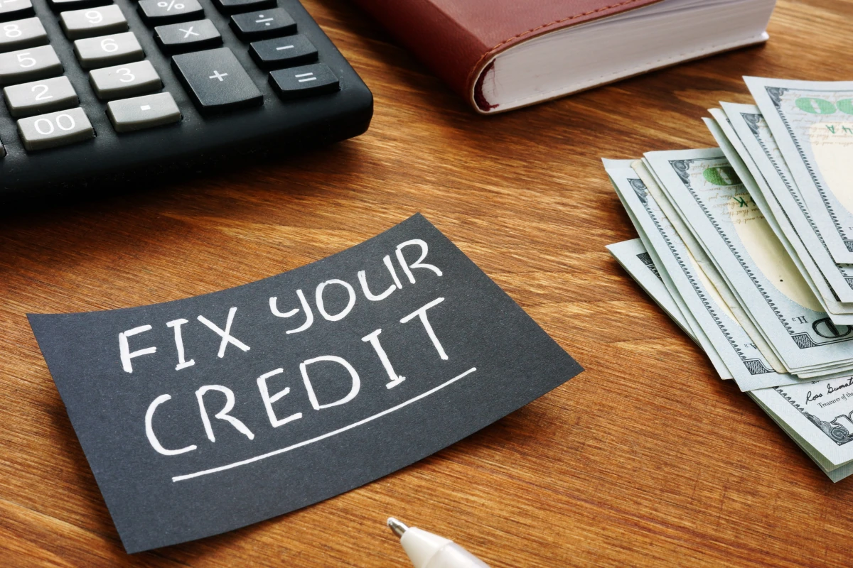 A stack of dollar bills, a calculator, and a note reading 'Fix Your Credit' placed on a wooden table, symbolizing actionable strategies to boost your credit score and achieve financial success.