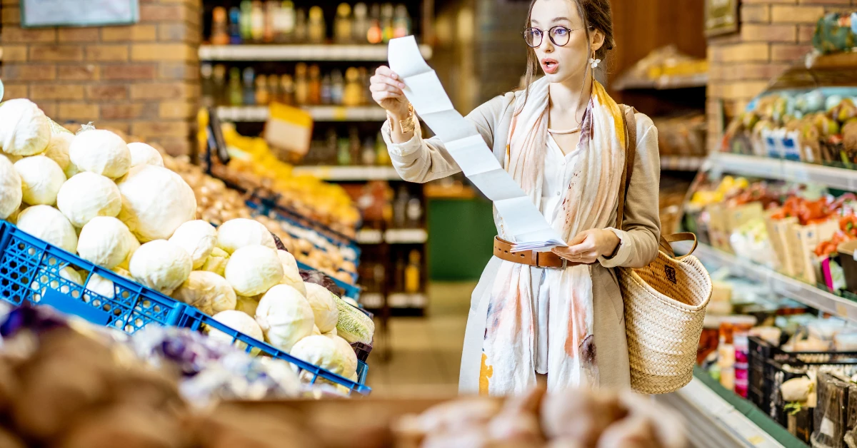 Shocked shopper holding a receipt in a grocery aisle obviously witnessing inflation impact in real time.