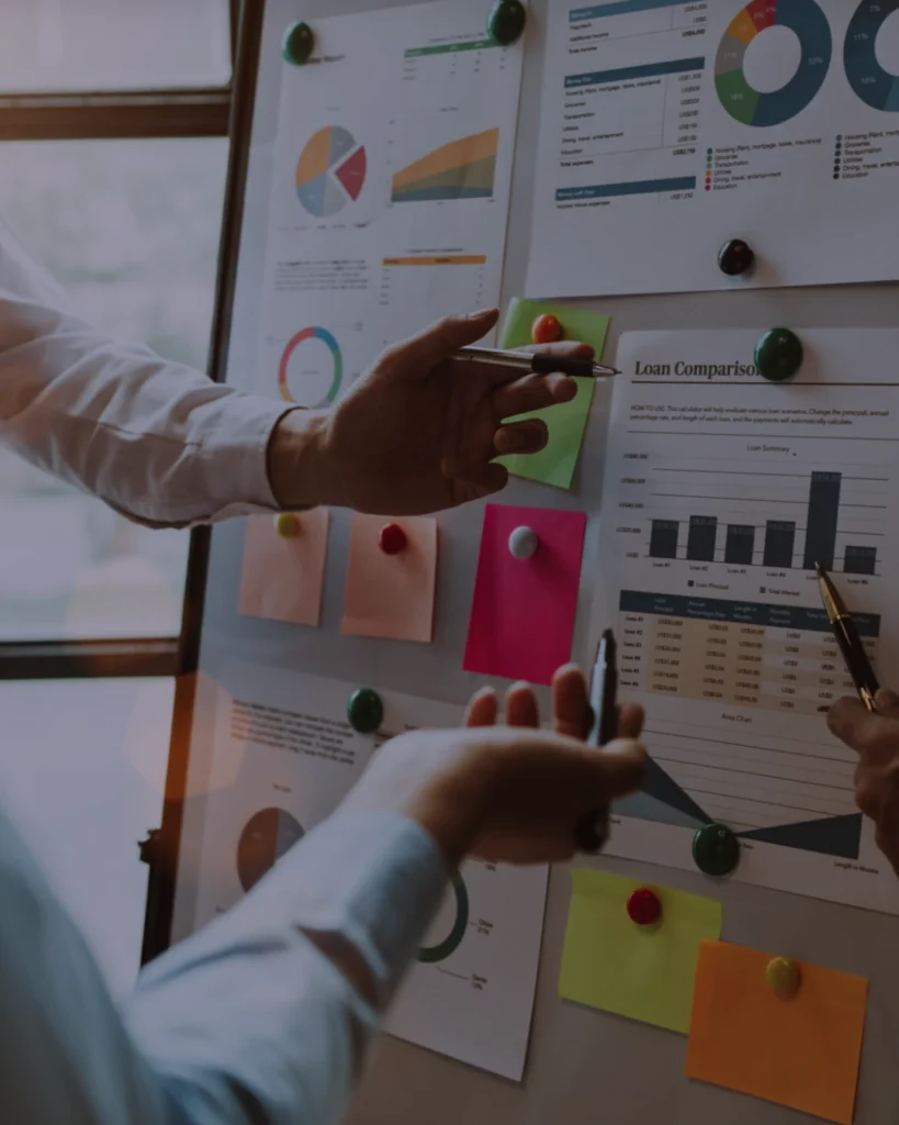 Two individuals pointing at charts on a board, discussing loan comparisons and trended data for consistent credit management.